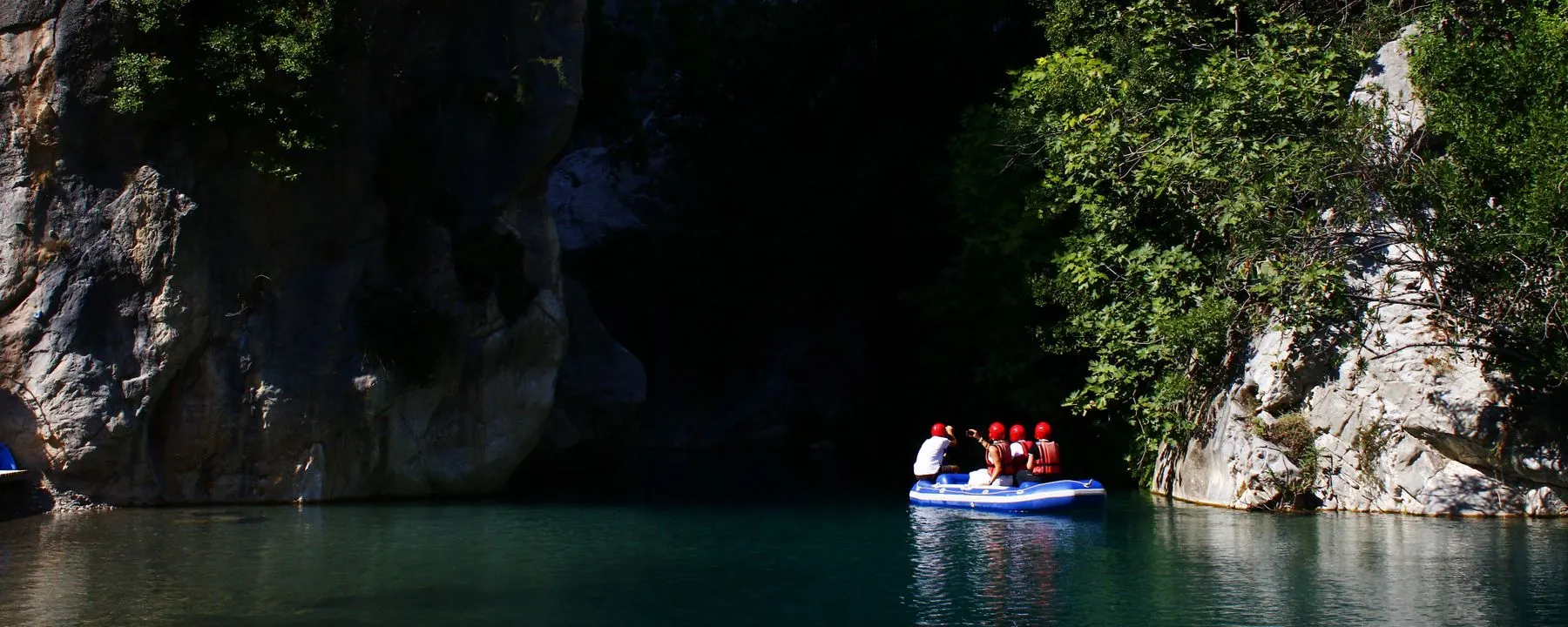 Un radeau et son équipage s'apprêtant à entrer dans une gorge sombre encaissée entre deux parois